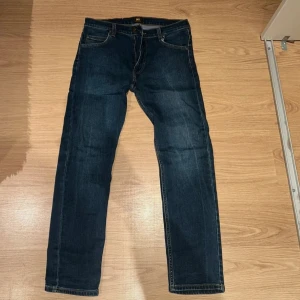 Mörkblå jeans från Lee W32 L30 - Säljer ett par mörkblå jeans från Lee med klassisk femficksdesign och raka ben. Jeansen har snygga kontrastsömmar och en läderpatch med Lee-loggan bak i midjan. Perfekta för dig som gillar en enkel och tidlös look. Mycket fina, använda någon enstaka gång 