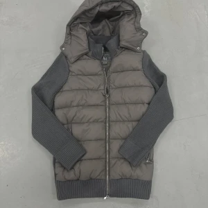 Marcel classic cardigan från Leon Marcel - Snygg grå pufferjacka från Leon Marcel med stickade ärmar och rygg, quiltad framsida och huva. Jackan har dragkedja framtill och ribbade muddar. Perfekt för dig som gillar en modern och clean look med extra komfort.