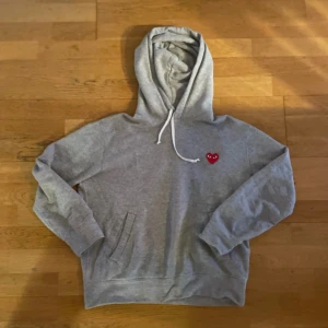  Comme des Garçons Play hoodie  - Grå hoodie från Comme des Garçons Play i storlek M. Tröjan är i fint skick och har inga skador. Skriv gärna vid fler du funderingar eller frågor.