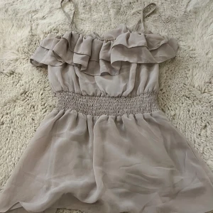 Beige volang linnetopp med smock - Supersöt beige linnetopp med tunna axelband och bred smock i midjan. Toppen har dubbla volanger upptill 