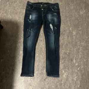Mörkblå skinny jeans från Bershka - Snygga mörkblå skinny jeans från Bershka med slitna detaljer och knappar framtill. Jeansen har klassisk femficksdesign, kontrastsömmar och en cool tvättad look. Passar dig som gillar en smal siluett och streetstyle.