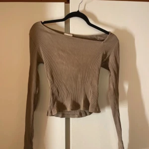 Beige ribbad långärmad topp - Säljer en beige ribbad topp med lång ärm och croppad passform. Toppen har en lätt offshoulder-skärning och är tillverkad i ett stretchigt material som sitter snyggt på kroppen. Perfekt att styla med jeans eller kjol för en trendig look.