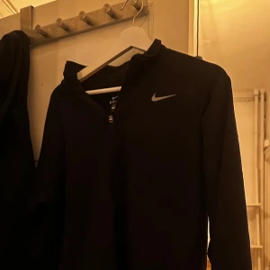 Svart Nike tröja med dragkedja Dri-fit - Svart hoodie från Nike med klassisk logga i silver på bröstet. Tröjan har hel dragkedja framtill och är långärmad, perfekt för träning eller daglig användning 