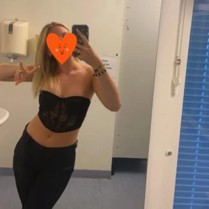 Svart spets bandeau korsett - Säljer en svart bandeau korsett med snygga spetsdetaljer framtill. Toppen är axelbandslös och har en croppad passform som framhäver midjan. Perfekt för dig som vill ha en trendig och edgy look. Spetsen ger en extra touch av stil.