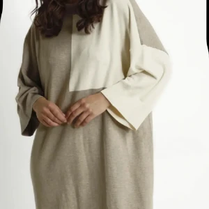 Beige och ljus stickad långklänning från danska Culture - Snygg stickad långklänning i beige och ljus färgblock med avslappnad passform och breda ärmar. Klänningen har rund halsringning och ett coolt grafiskt mönster framtill. Perfekt för dig som gillar en loose och chill stil. NY