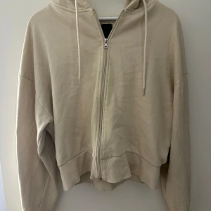 Beige hoodie med dragkedja från 157 - Säljer en beige hoodie från 157 i storlek L/XL. Tröjan har huva med snörning, hel dragkedja framtill och ribbade muddar vid ärmslut och nederkant. Perfekt för chill dagar och enkel att matcha med jeans eller mjukisbyxor.