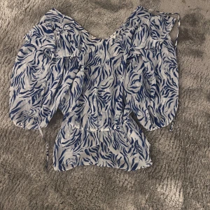 Blåvit blus med zebramönster - Säljer en luftig blus i blått och vitt med zebramönster. Blusen har voluminösa ärmar och v-ringad hals. Materialet är tunt och känns som polyester, perfekt för varmare dagar. Midjan är markerad med en lätt rynkning. 