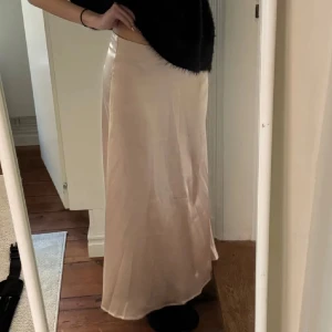Champagnefärgad satinlångkjol - Säljer en elegant långkjol i champagnefärgad satin med slät och glansig yta. Kjolen har en rak och flowy passform som sitter snyggt i midjan. Perfekt för dig som gillar stilrena och lyxiga vibes. Fråga gärna om fler bilder eller mått!