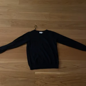 En mörkblå stickad tröja från VILA - En mörkblå stickad tröja från VILA med rund hals och ribbade muddar. Tröjan har en klassisk, enkel design och är långärmad, perfekt för att hålla dig varm under kyliga dagar. Passar dig som gillar stilrena och tidlösa plagg.