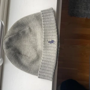 Grå merinoullsmössa Polo Ralph Lauren - Snygg grå mössa från Polo Ralph Lauren i 100% merinoull. Klassisk ribbad kant och broderad logga framtill. Perfekt för kalla dagar och enkel att matcha med olika outfits. Köpt för 800kr