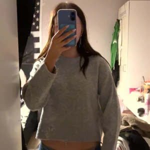 Grå stickad croppad tröja - Mysig grå stickad tröja med croppad passform och breda ribbade muddar vid ärmslut och nederkant. Perfekt för lager-på-lager och chill dagar. Rund halsringning och lång ärm ger en enkel men snygg look.