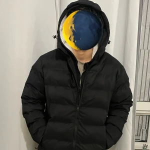 Svart pufferjacka från H&M med huva - Svart pufferjacka från H&M i storlek S. Jackan har en rejäl huva med dragsko, breda quiltade sektioner och dragkedja framtill. Perfekt för kalla dagar och har en clean, modern look som funkar till de flesta outfits.