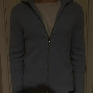 Ljusblå stickad kofta från Ljung - Säljer en ljusblå stickad kofta från Ljung by Marcus Larsson. Koftan har hel dragkedja framtill, ribbad struktur och hög krage. Perfekt för lager-på-lager och chill stil. Passar dig som gillar enkel men snygg design.