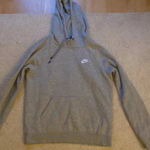 Grå hoodie från Nike med huva - Säljer en grå hoodie från Nike med klassisk logga på bröstet. Tröjan har huva med snörning och en stor magficka framtill. 