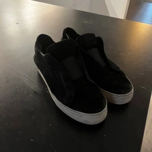Axel Arigato - Svarta slip-on sneakers från Axel Arigato med en stilren och minimalistisk design. Skorna är slitna i hälen men och lite på utsidan.