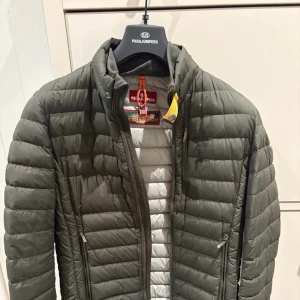 Grön dunjacka från Parajumpers - Säljer en grön dunjacka från Parajumpers med quiltad design och dragkedja framtill. Jackan har ståkrage, sidofickor med dragkedja och en patch med logga på ärmen. Perfekt för kyliga dagar och har en snygg, sportig look.