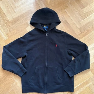 Ralph Lauren zip Hoodie - äkta, bra skock! - Klassisk svart hoodie från Polo Ralph Lauren med röd logga. Äkta (se bild på lapp). Mjuk, bekväm och passar till allt. Inga hål, inga fläckar – riktigt fint skick.  Storlek: XL i barn = S i herr Nypris runt 1600 kr  💨 Säljer för 500– kan gå ner lite vid snabb affär. 📦 Skickas direkt. 