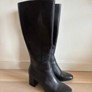 Svarta stövlar med klack och dragkedja - Säljer ett par svarta stövlar i skinn med klack på ca 6 cm. Stövlarna har dragkedja på insidan för enkel på- och avtagning. Stilrena och passar perfekt till höst och vinter. Klassisk modell med platt sula och elegant look.