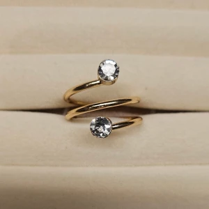 Guldfärgad spiralring med stenar - Trendig spiralformad ring i guldfärg med två gnistrande klara stenar i varje ände. Snygg och modern design som verkligen sticker ut och ger en lyxig känsla till din look.