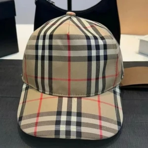 Burberry keps - Snygg keps med klassiskt rutigt mönster i beige, svart, vitt och röda linjer. Perfekt accessoar för en trendig och stilren look. Justerbar baktill för bästa passform.