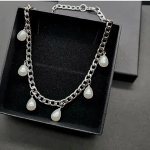Silverhalsband med pärldroppar - Stilrent halsband i silverfärgad metall med grov kedja och sex hängande droppformade pärlor. Material-rostfritt stål 