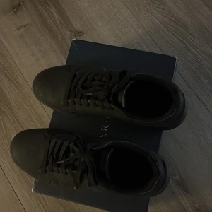 Skor - Snygga helsvarta sneakers från Pier one med klassisk rund tå och platt sula. Skorna har snörning och är tillverkade i ett slätt syntetmaterial som ger en clean och stilren look. Perfekta för dig som gillar minimalistisk stil och vill ha ett par diskreta sneakers. Skorna är använda ett fåtal gånger, original box följer med! 