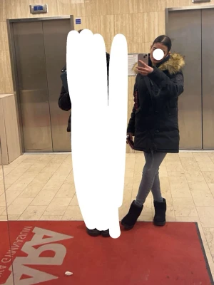 Svart parkasjacka med fuskpäls - Säljer en svart parkasjacka med stor huva och fuskpäls i brunt/gult. Jackan har dragkedja och knappar framtill samt flera fickor. Perfekt för kalla dagar och har en snygg, klassisk look.