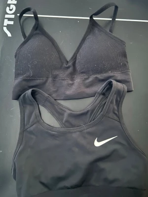 Svarta bhar, Nike sport-bh & ribbad bh - Två svarta bhar, en sport-bh från Nike med klassisk logga och brottarrygg i slät funktionsmaterial, samt en ribbad bh med smala axelband och v-ringning. Perfekta för träning eller chill. Snygg och enkel design. Den ribbade är från shein 