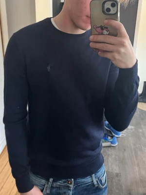Mörkblå merinoull tröja från Ralph lauren - Snygg mörkblå tröja från Ralph Lauren med rund halsringning och diskret broderad logga på bröstet. Tröjan har en klassisk passform och är perfekt att matcha med jeans. Trröjan är i bra skick men finns några små defekter