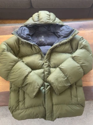 Olivgrön dunjacka från Haglöfs - Säljer en olivgrön dunjacka från Haglöfs med huva och dragkedja. Perfekt för vintern och kalla dagar. Storlek S 