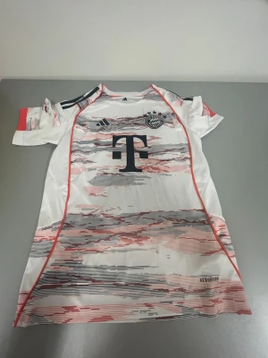 Bayern München matchtröja Adidas - Säljer en vit och röd Bayern München matchtröja från Adidas med korta ärmar. Tröjan har digitalt mönster i rött och grått, klubbmärke och Adidas-logga på bröstet samt FC Bayern München-tryck på ryggen. Tillverkad i lätt funktionsmaterial.