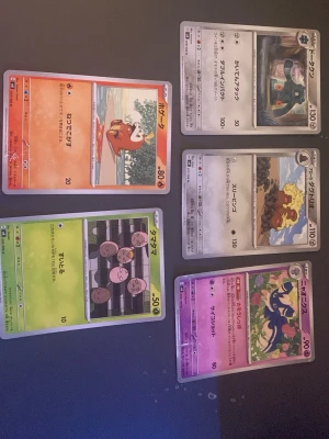 Pokémonkort japanska, 5 st - Säljer ett set med 6 japanska Pokémonkort i olika färger och motiv. Korten har illustrationer av olika Pokémon och text på japanska. Färgerna varierar mellan röd, grön, lila och grå. Perfekt för samlare eller Pokémonfans som vill utöka sin samling.