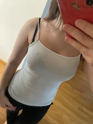 Två baslinnen i vitt och grått - Säljer två stilrena baslinnen, ett vitt och ett ljusgrått. Båda har smala axelband och är figurnära i modellen.Materialet känns mjukt och stretchigt, troligen bomull med lite elastan.