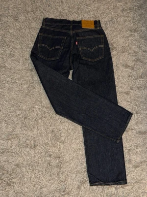 Mörkblå Levi's jeans - Säljer ett par mörkblå jeans från Levi's 30/30 med raka ben och klassiska bakfickor med gul kontrastsöm. Perfekta för dig som gillar en tidlös och clean look. Ny pris 1200kr, Helt nya utan prislapp endast testade! 
