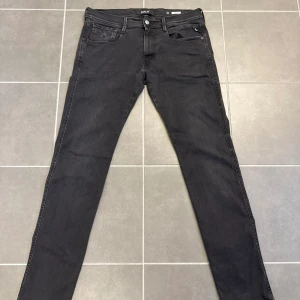 Svarta jeans från Replay - Snygga svarta slim fit jeans från Replay, modell Anbass. Jeansen har klassisk femficksdesign, svarta sömmar och diskret Replay-logga vid fickan. Perfekta för dig som gillar en stilren och modern look.