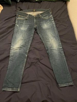 Lee jeans  - Säljer ett par blå slim fit jeans från Lee i storlek W34/L32 med klassisk femficksdesign och snygga slitningar framtill. Jeansen har en skön passform och är tillverkade i denim. Perfekta till en avslappnad stil 