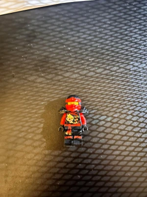 LEGO Ninjago röd ninjafigur - Säljer en LEGO Ninjago minifigur föreställande en röd ninja med svarta och guldiga detaljer. Figuren har rött huvudskydd, svarta ben och armar samt tryck med drakmotiv på överkroppen. Perfekt till samlingen eller lek!