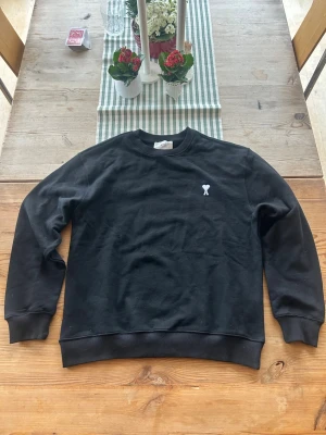 Svart sweatshirt från Ami Paris - Svart sweatshirt från Ami Paris med klassisk rund halsringning och ribbade muddar. På bröstet finns det ikoniska hjärta-A broderiet i vitt. Perfekt för en clean och stilren look.