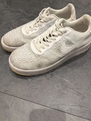 Vita Nike Flyknit sneakers - Säljer ett par vita Nike sneakers med Flyknit-överdel och klassisk swoosh på sidan. Skorna har lågt skaft, vita snören och en lätt, flexibel sula. Perfekta för dig som gillar stilrena och bekväma sneakers.