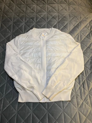 Vit quiltad cardigan med dragkedja - Snygg vit cardiganjacka med quiltad framsida och stickade ärmar. Jackan har dragkedja framtill, ribbade muddar och fickor på sidorna. Perfekt för lager på lager och ger en clean look. Den är i storlek 170/xs-s.  Tveka inte på att ställa frågor eller be om fler bilder. 