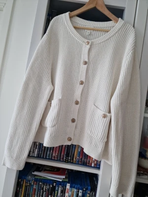 H&M cremefärgad / vit stickad kofta med guldknappar - Snygg H&M creme eller vit stickad kofta med rund halsringning och stora guldknappar framtill. Koftan har två praktiska fickor med knappdetalj och är gjord i ett tjockare, ribbstickat material. Perfekt för lager-på-lager och chill vardagsstil. Storlek XXL. Använd endast en gång, perfekt skick. Mycket bra kvalitet.