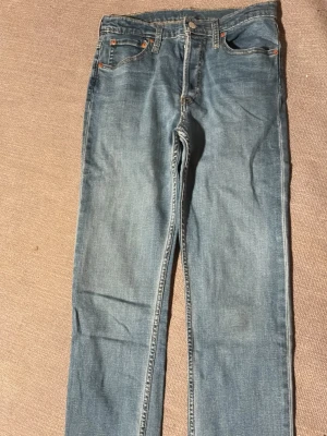 Levi's 501 klassiska blå jeans - Klassiska blå Levi's 501 jeans med rak passform och fem fickor. Jeansen har knappgylf och är tillverkade i slitstark denim. Perfekta för dig som gillar tidlös stil och vill ha ett par ikoniska jeans i garderoben.