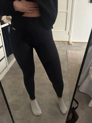 Svarta leggings från Stronger - Säljer ett par svarta leggings från Stronger med hög midja och stretchigt material. De har en tight passform och en diskret logga på höften. Perfekta för träning eller chill dagar. Sömnen har gått sönder lite baktill men leggingsen har ej något hål.