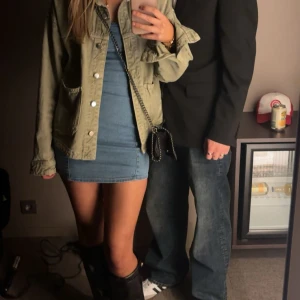 Blå jeansklänning med kort längd - Trendig blå jeansklänning med kort längd och figurnära passform. Klänningen är ärmlös och har en enkel, stilren design som passar perfekt till boots och accessoarer.