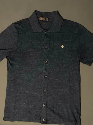 Mörkblå kortärmad skjorta från Morris - Snygg mörkblå skjorta från Morris med korta ärmar och klassisk krage. Skjortan har knäppning framtill och en liten broderad detalj på bröstet. Tillverkad i ett mjukt och lätt material som känns bekvämt mot huden.