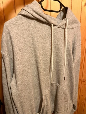Grå basic hoodie med huva - En stilren grå hoodie med huva och dragsnören. Klassisk känguruficka framtill och ribbade muddar vid ärmslut och nederkant. Perfekt för en avslappnad look.