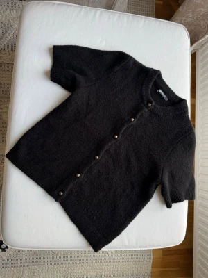 Svart kortärmad kofta med pärlknappar - Snygg svart kofta från Gina tricot  med korta ärmar och rund hals. Koftan har dekorativa pärlknappar framtill och är stickad i ett mjukt material. Perfekt att styla över en topp eller klänning.