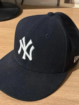 Mörkblå New Era Yankees keps - Snygg mörkblå keps från New Era med klassiska New York Yankees-loggan broderad i vitt framtill. Kepsen har böjd skärm.