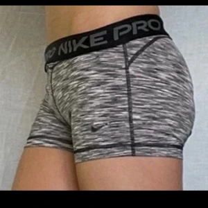 Nike Pro Dri-Fit träningstights shorts - Nike Pro Dri-Fit shorts i tight modell, perfekt för träning. De är gråmelerade med svart resår i midjan där det står 'NIKE PRO'. Materialet är stretchigt och andas, vilket gör dem riktigt sköna under intensiva pass.