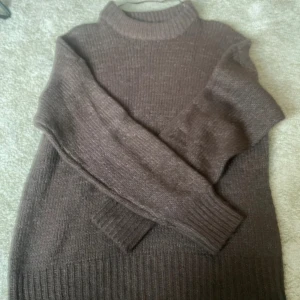 Brun stickad polotröja - Mysig brun stickad polotröja från lager 157 med ribbade muddar och hög krage. Perfekt för kyliga dagar och enkel att matcha med jeans eller kjol. Klassisk modell med lång ärm och relaxed fit.